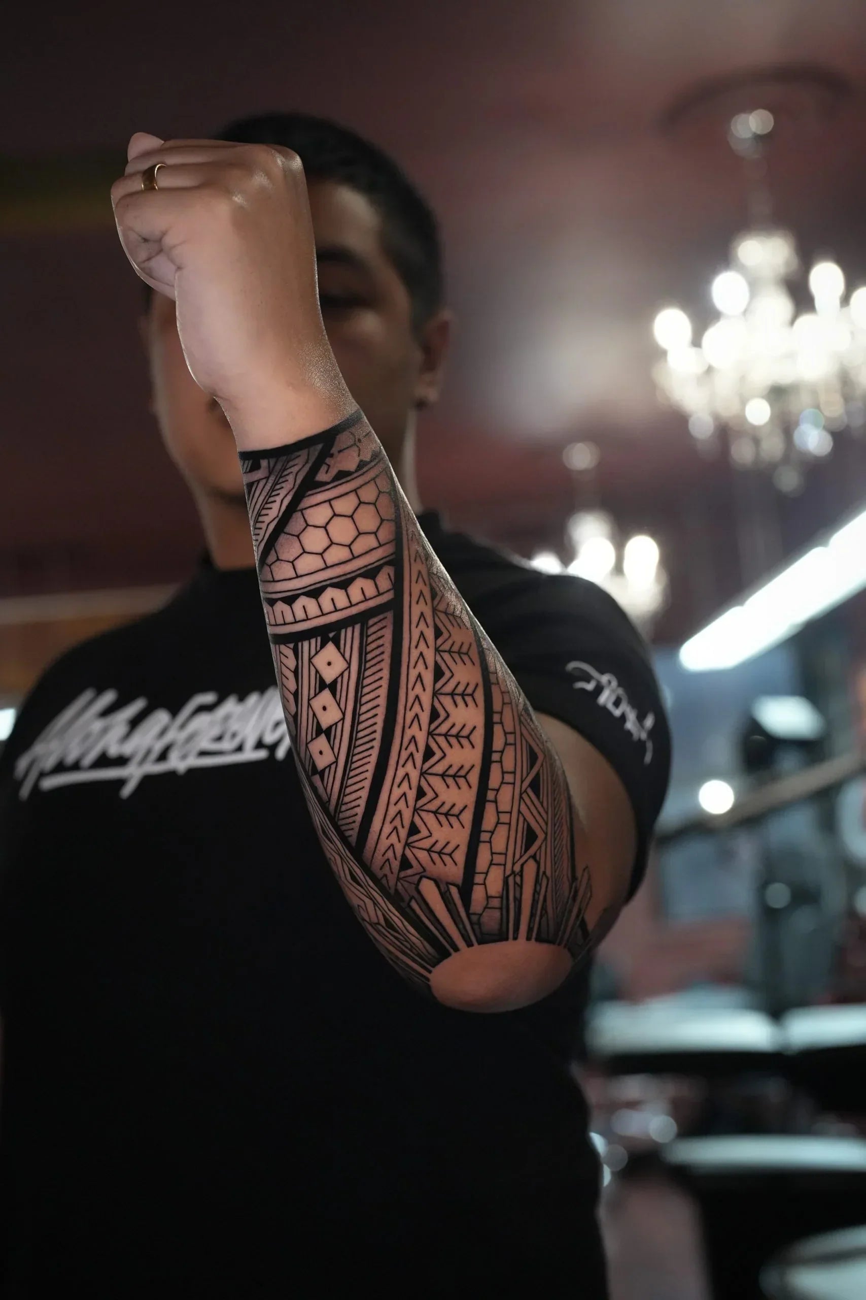 A black ink geometric forearm tattoo showing intricate tribal patterns, line work, and a prominent sun motif wrapping around the elbow.