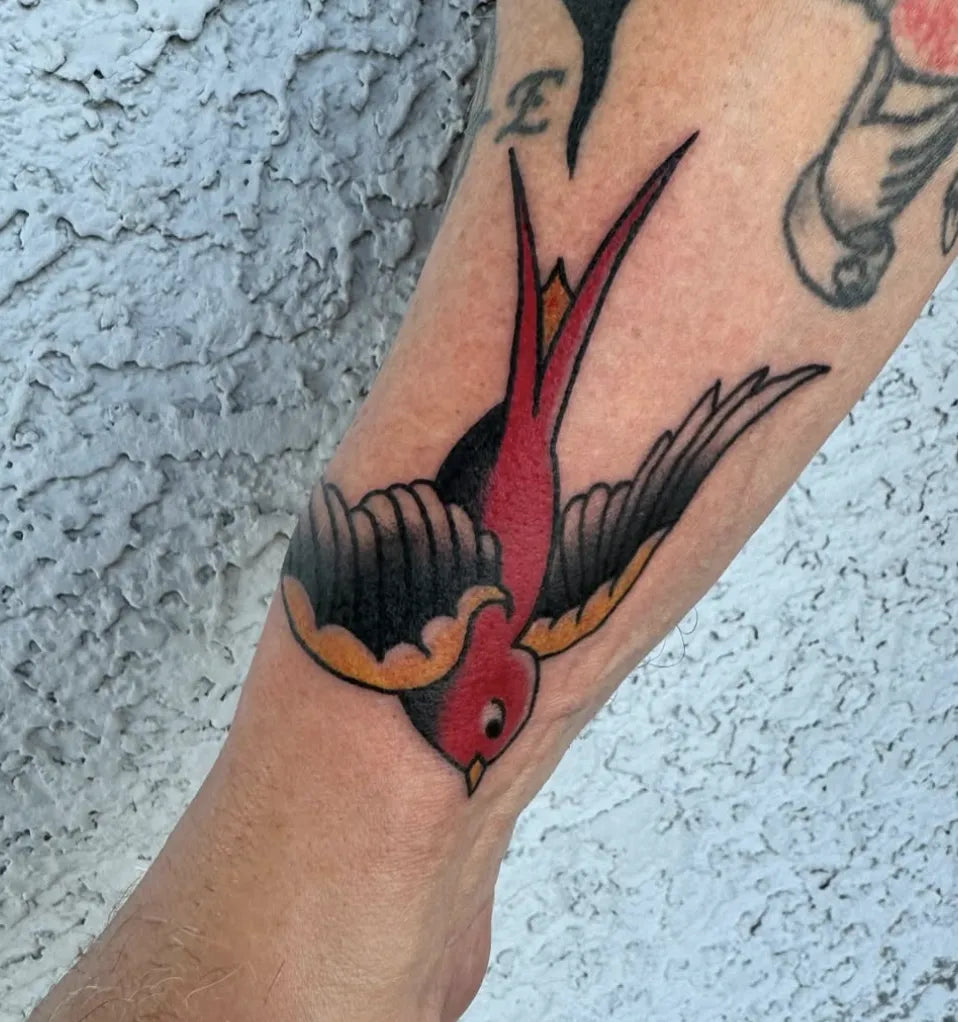 American Traditional swallow tattoo in flight featuring a red chest, black wings, and yellow accents.