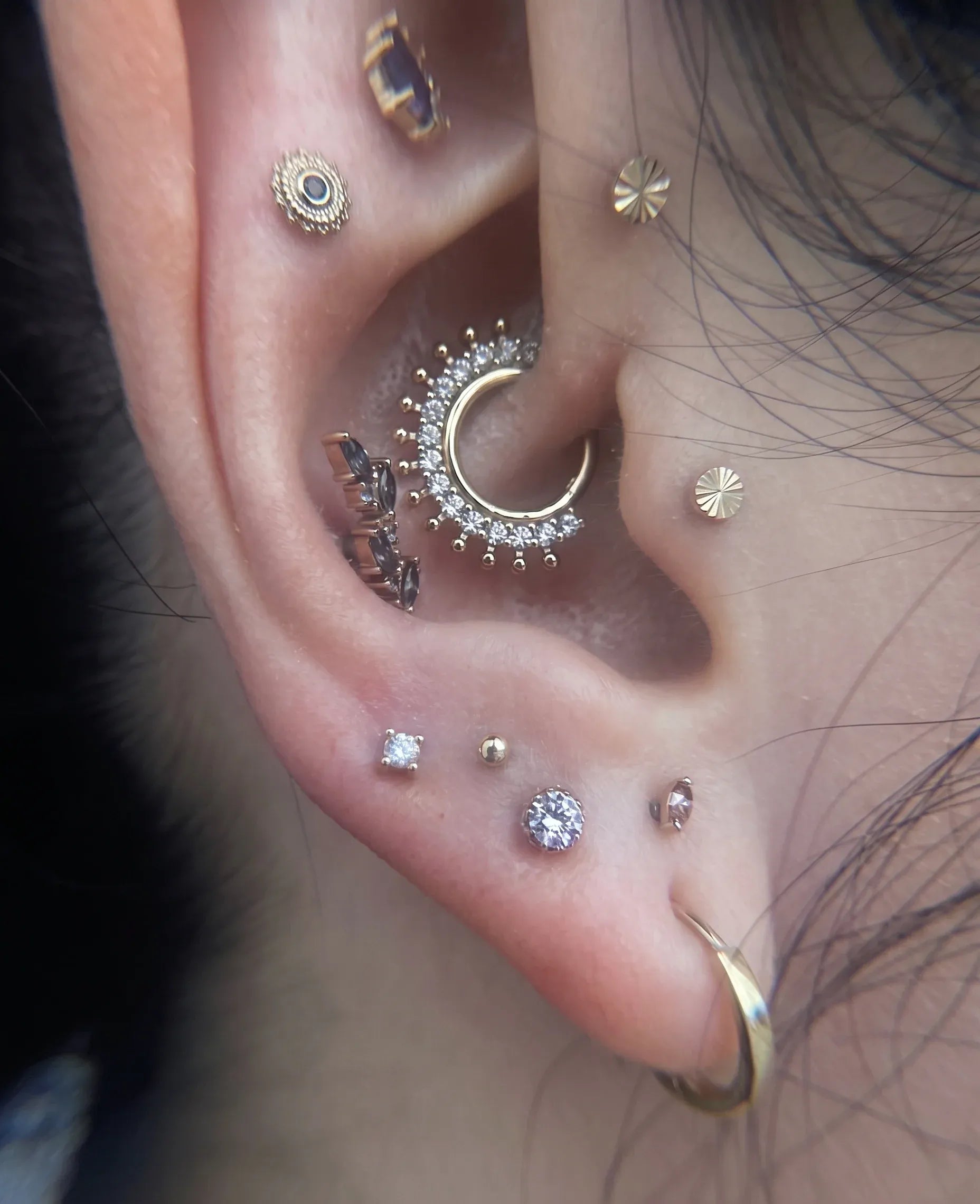 Curated ear curation featuring gold studs, a gem-encrusted daith hoop, and stacked earlobe piercings.