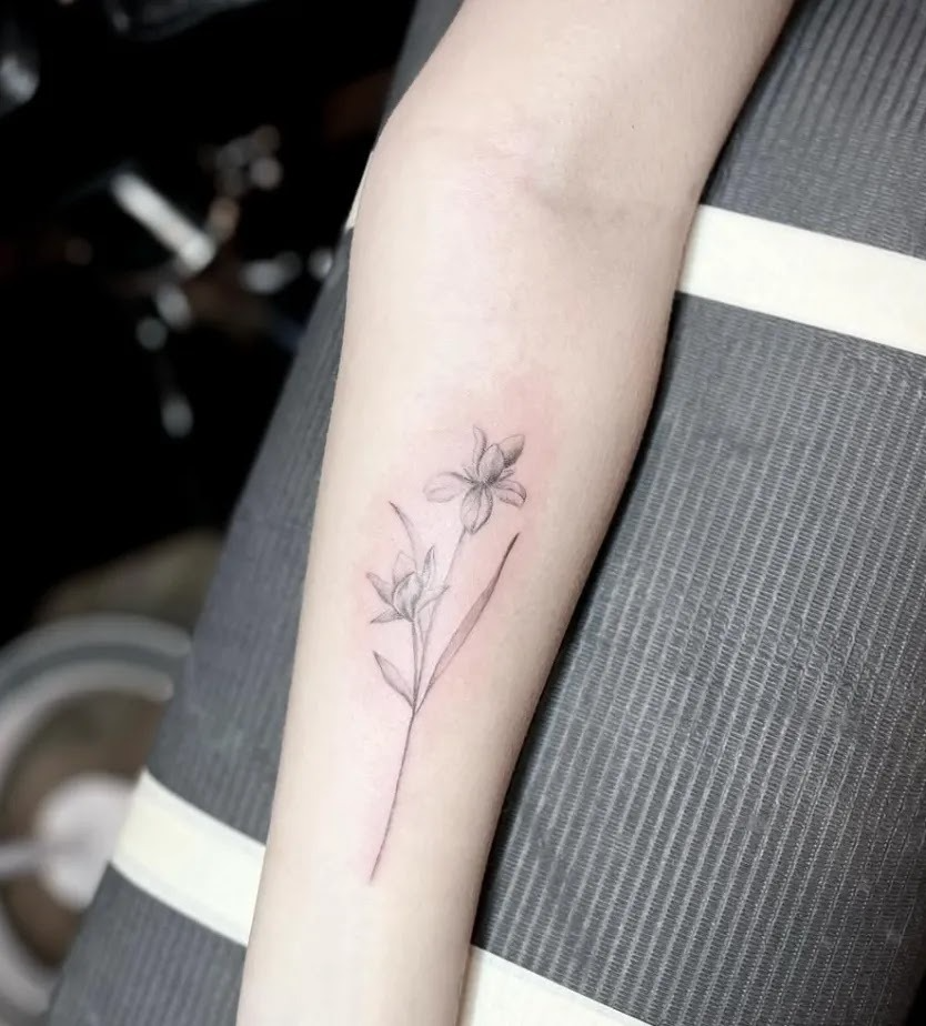 Minimalist fine line floral tattoo on the forearm with soft shading and thin black lines.