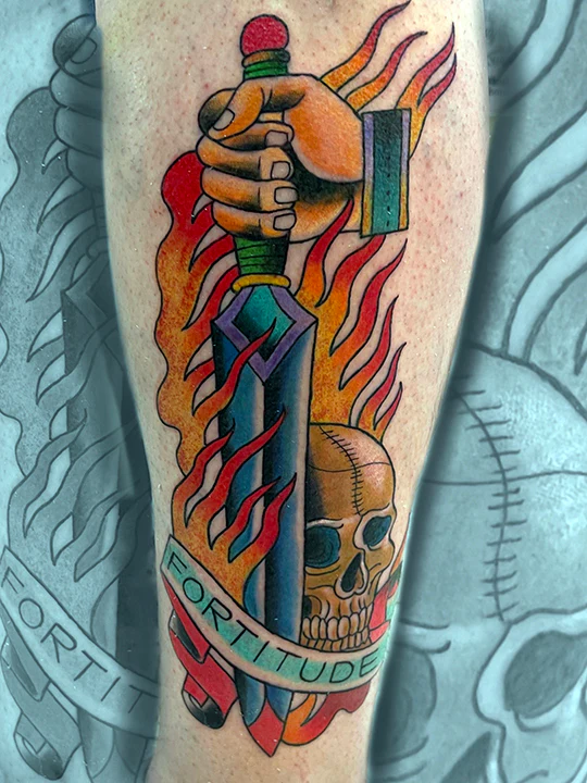 Color tattoo of a hand gripping a dagger wrapped in flames, with a skull and banner reading “Fortitude,” done in bold traditional tattoo style.