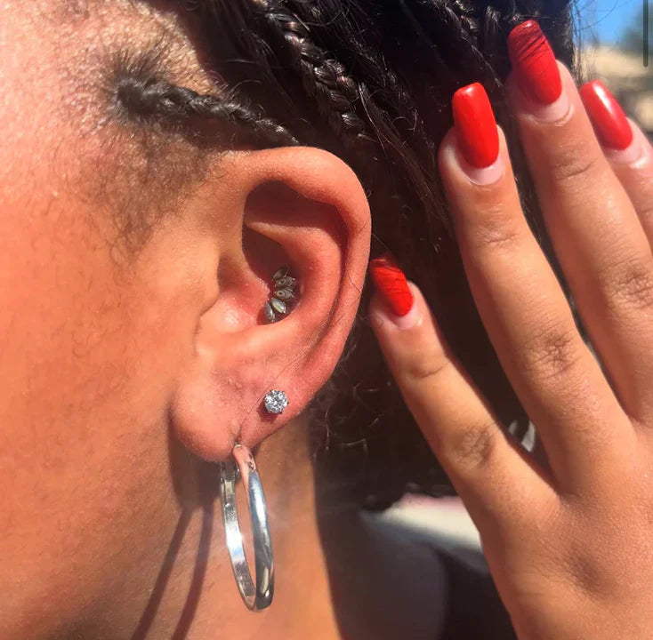 Close-up of a healed conch piercing featuring an ornate fan-shaped marquise cluster jewelry design next to a classic silver lobe hoop