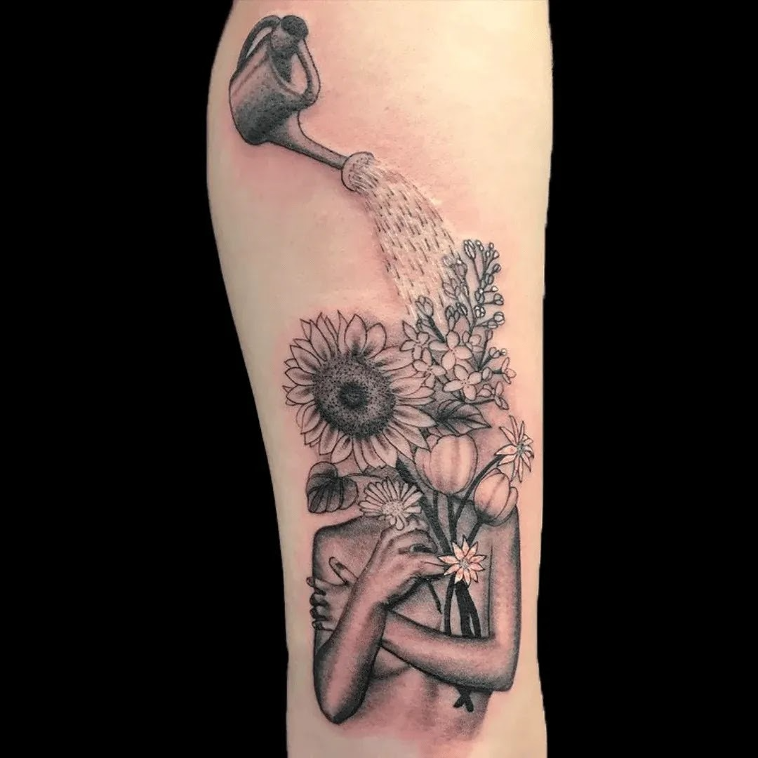 Black and grey surreal tattoo of a human figure with flowers growing from the head, including sunflowers and botanical elements with soft shading.