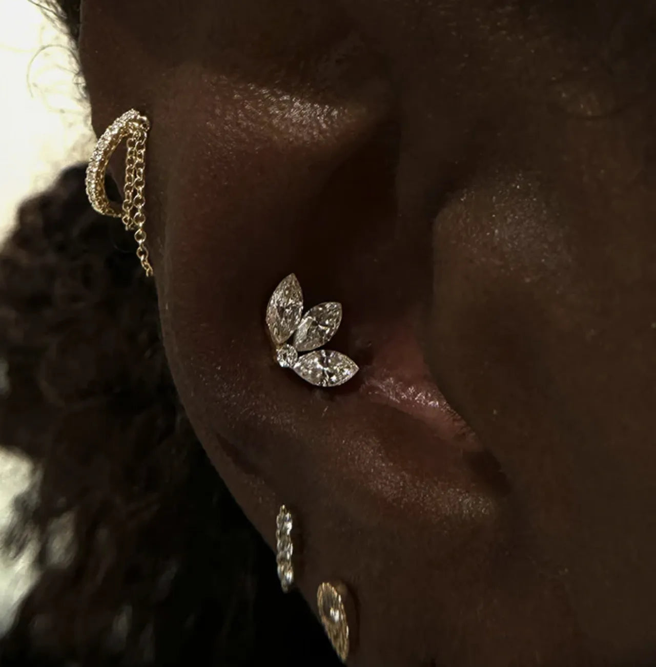 Close-up of a face featuring a silver septum ring, a gold stud with a green stone on the upper lip, and a textured gold disk on the lower lip.