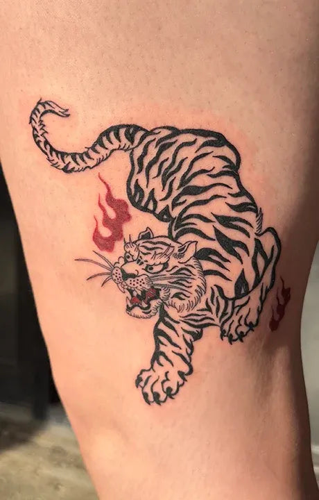 Fine-line blackwork tattoo of a snarling tiger in a dynamic pose with small red flame accents.