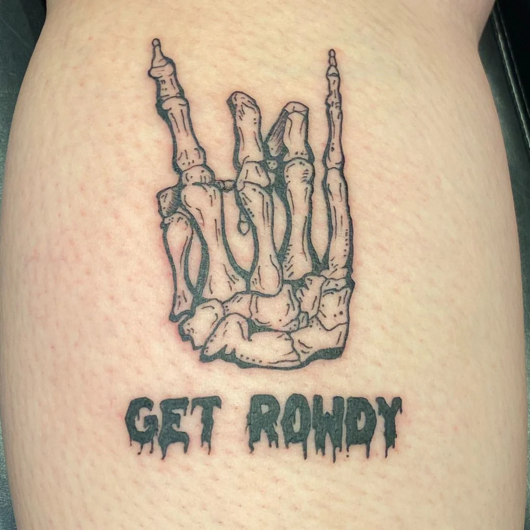 Black and grey tattoo of a skeletal hand making a rock hand gesture, with dripping gothic-style lettering below that reads “Get Rowdy.”
