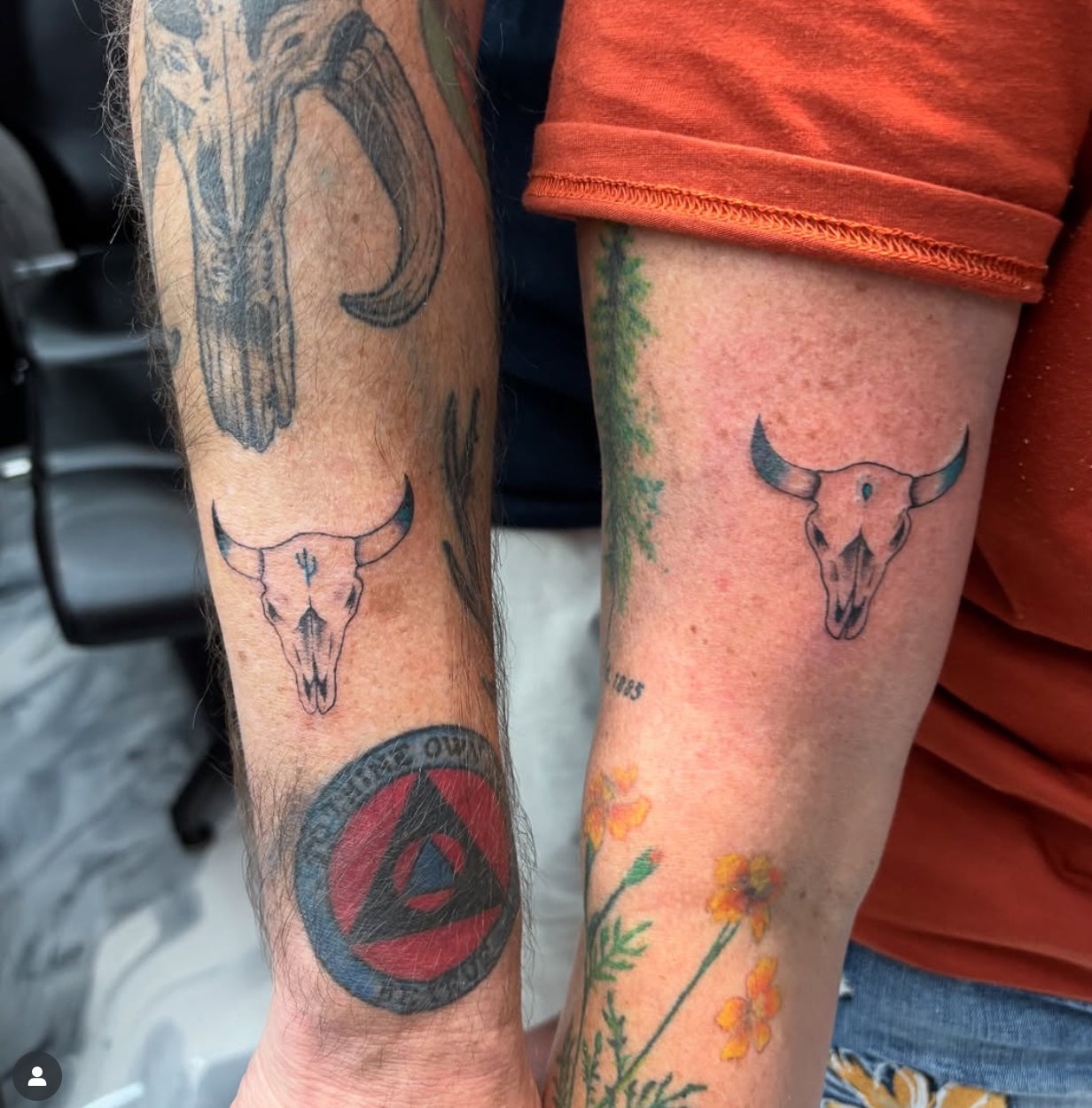 Two forearms with matching bull skull tattoos. Each tattoo shows a simple linework steer skull placed near the wrist.